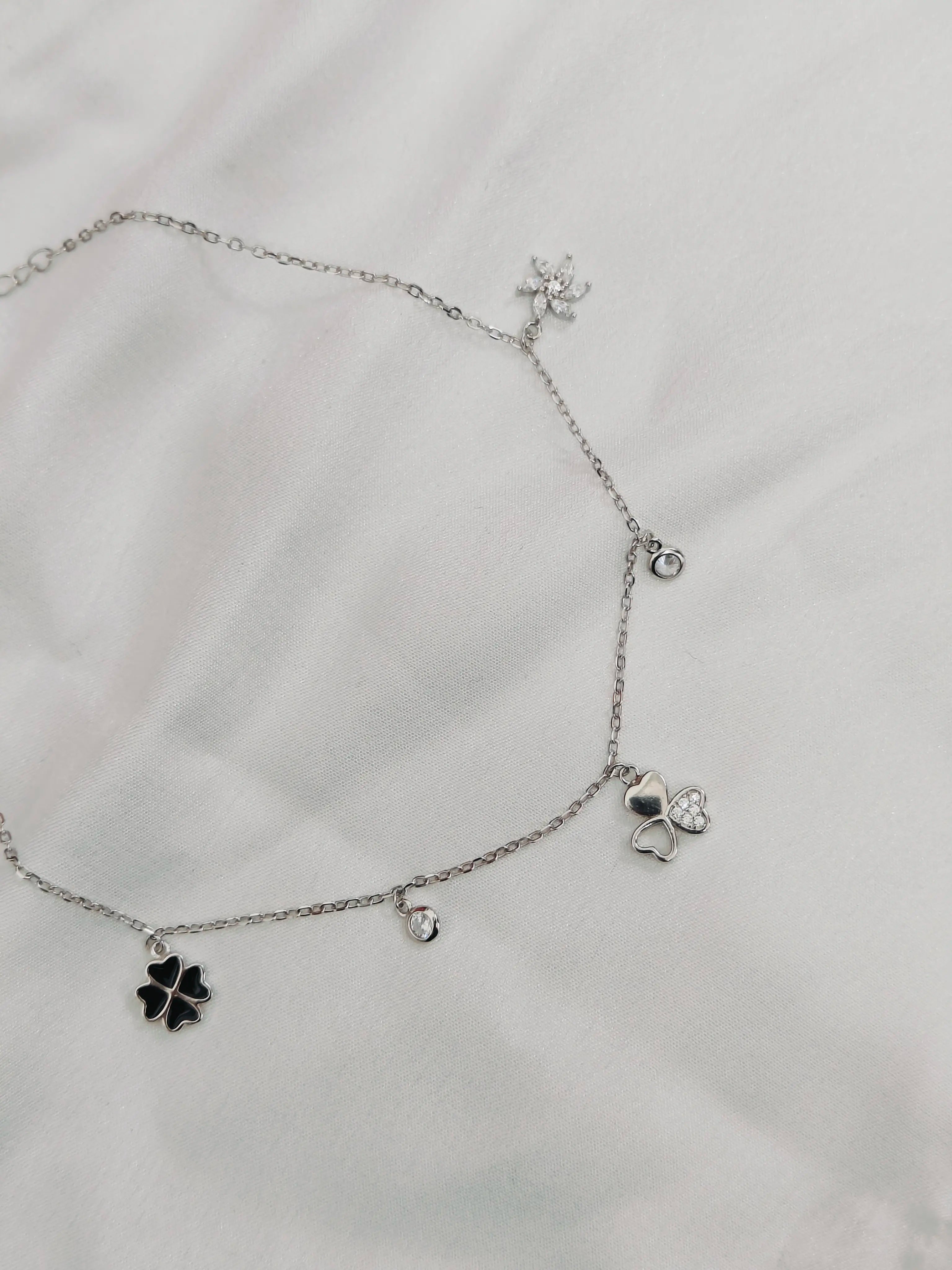 Silver necklace with clover-shaped charms on a light gray background